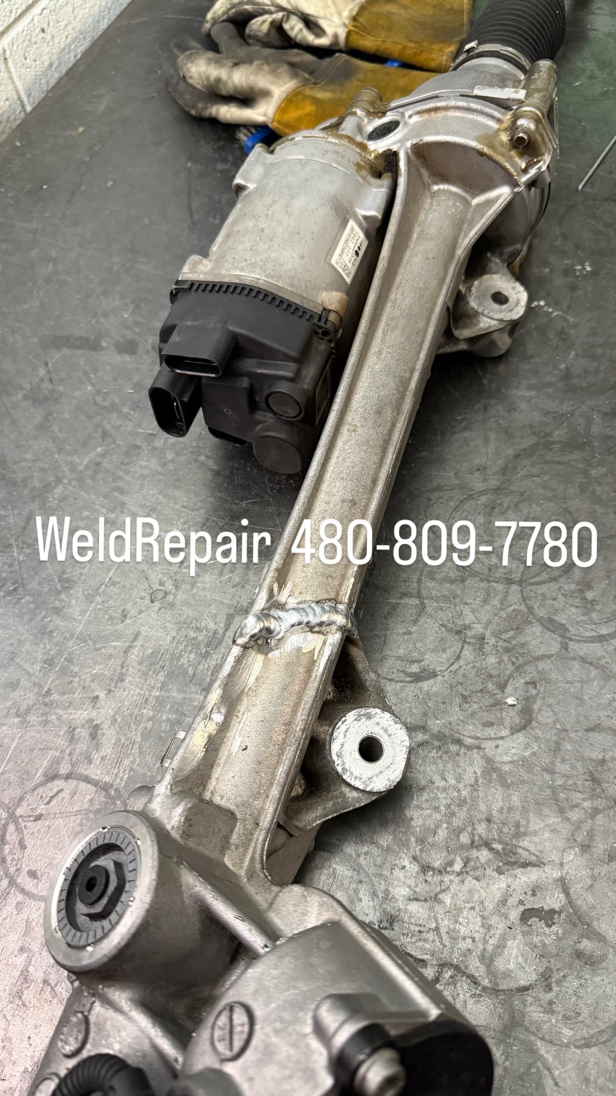 Aluminum electric power steering rack featuring a fresh weld repair bead on a metal workbench.