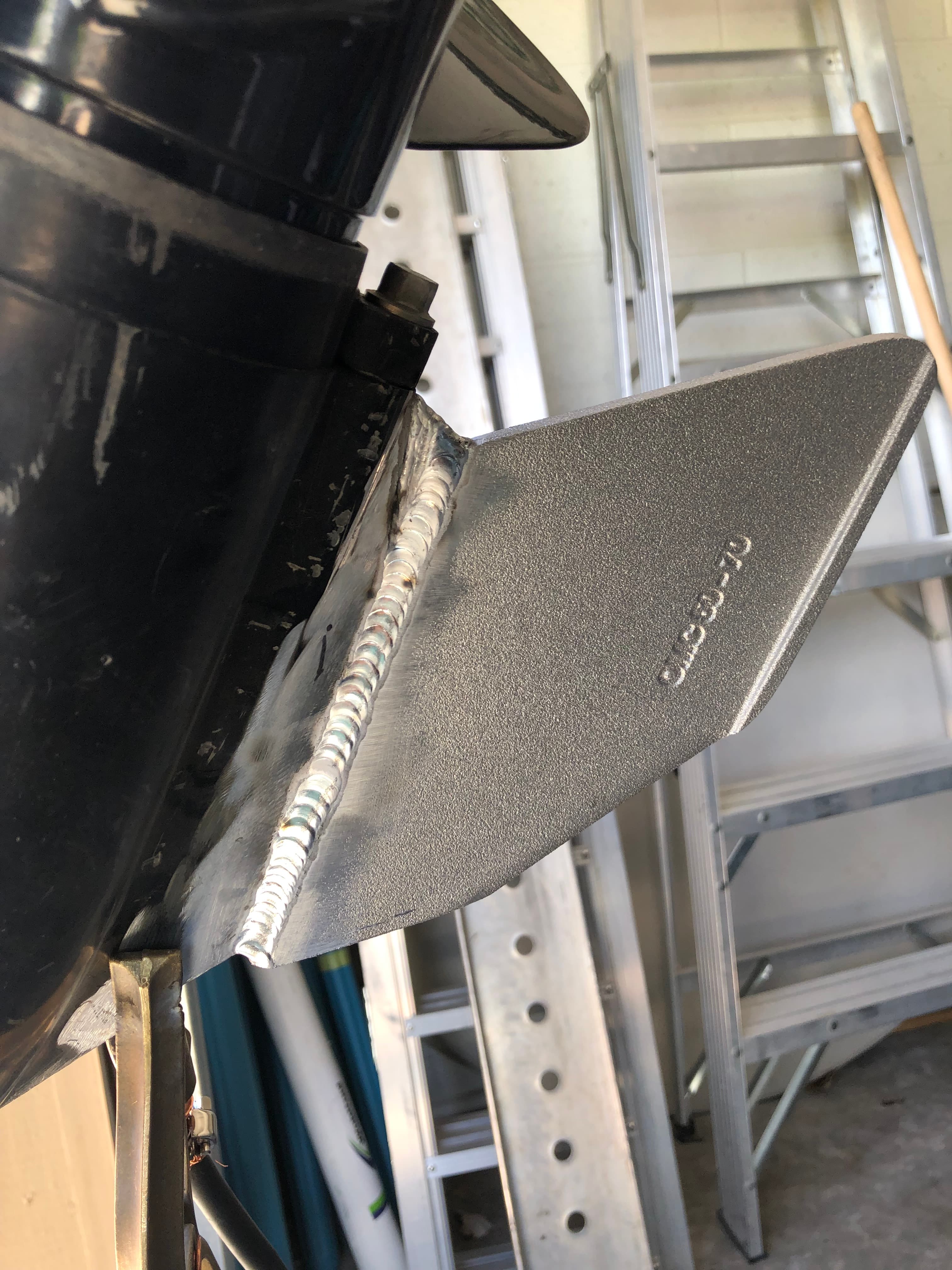Professional aluminum weld bead connects a new replacement skeg to a black outboard motor unit.