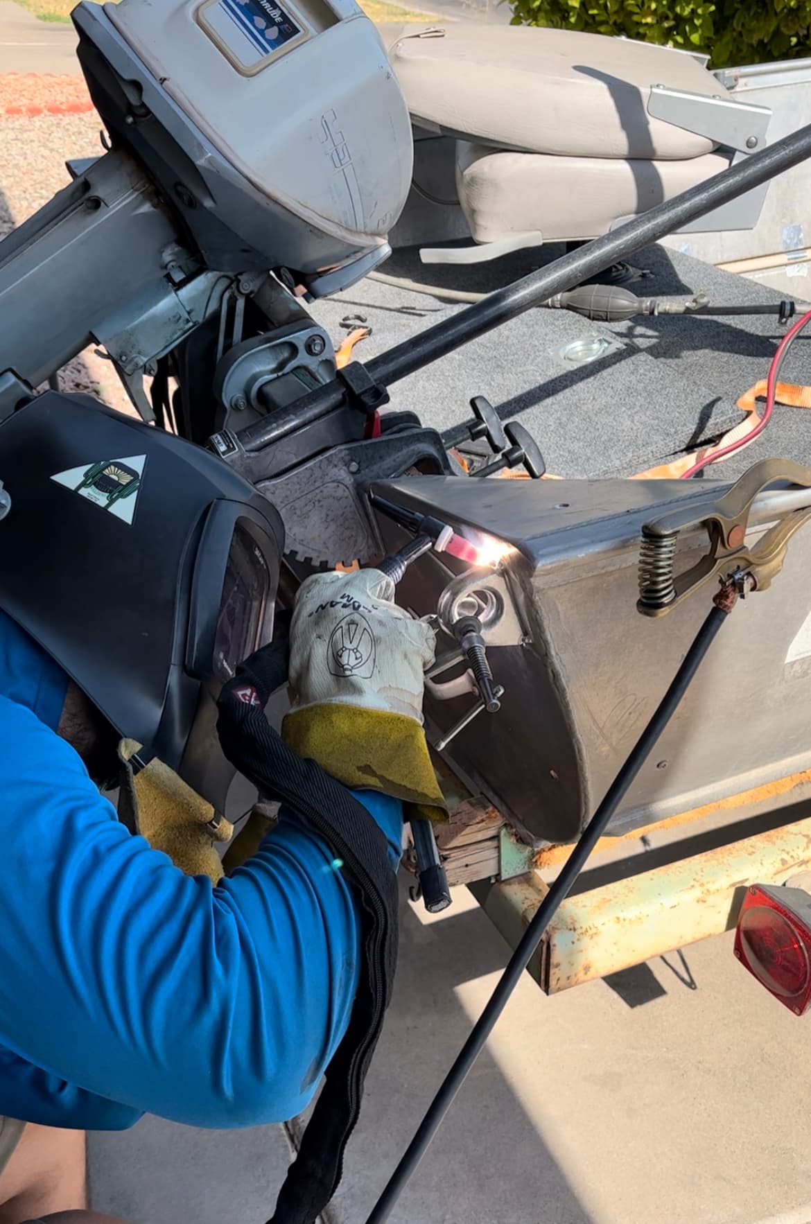 Person wearing a welding mask and gloves welds the metal hull of a boat.